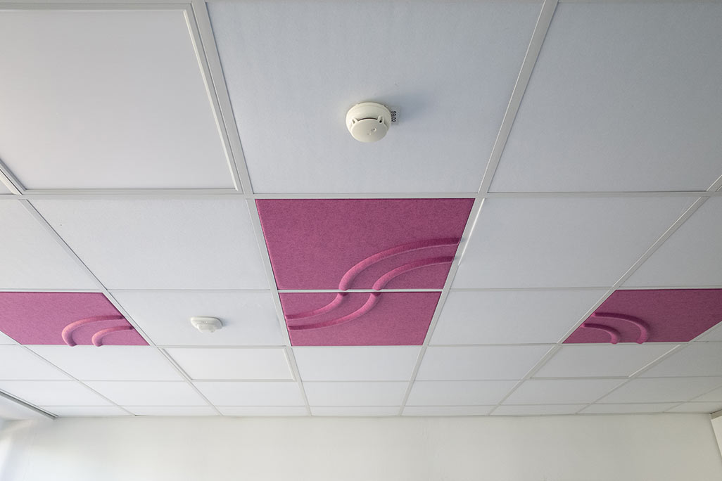 Ausschnitt einer handelsüblichen Rasterdecke mit eingelegten Akustikabsorbern soni COMFORT SD in Weiß und soni COLOR Design in Pink.