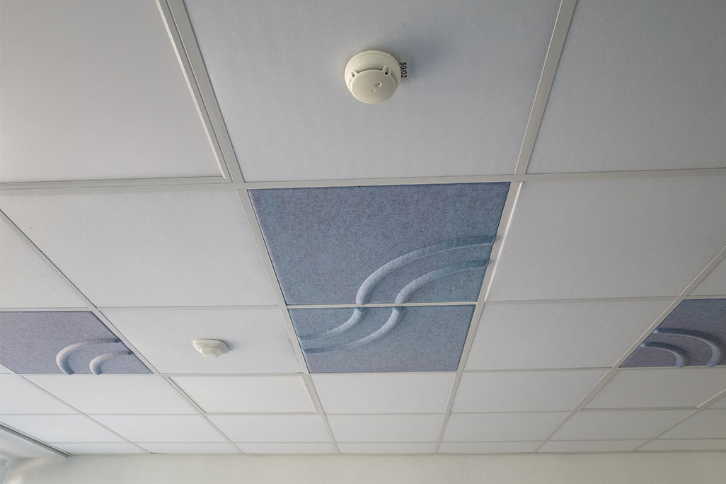 Ausschnitt einer handelsüblichen Rasterdecke mit eingelegten Akustikabsorbern soni COMFORT SD in Weiß und soni COLOR Design in Blau.