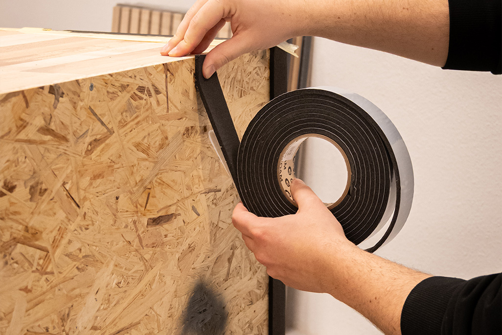 Schaumstoffband wird auf Rückwand eines Regals geklebt